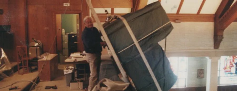 Charlie Meade steadying a strapped, blanket-wrapped piece in a wood-beamed hall