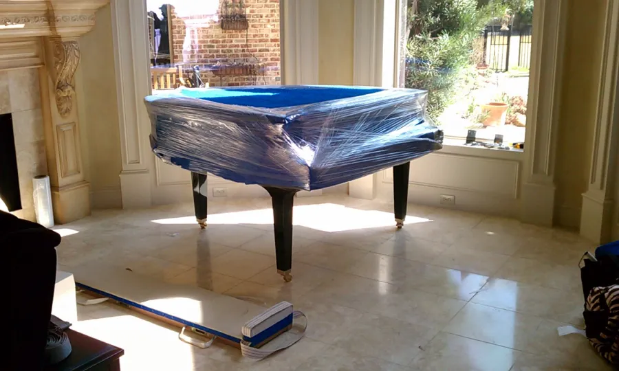 Grand piano shrink-wrapped and ready to move in a marble-floored room
